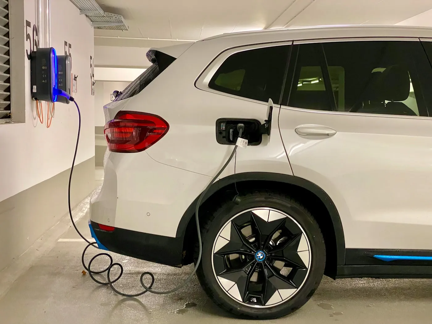 A white electric SUV charging from a wall charger in a parking garage
